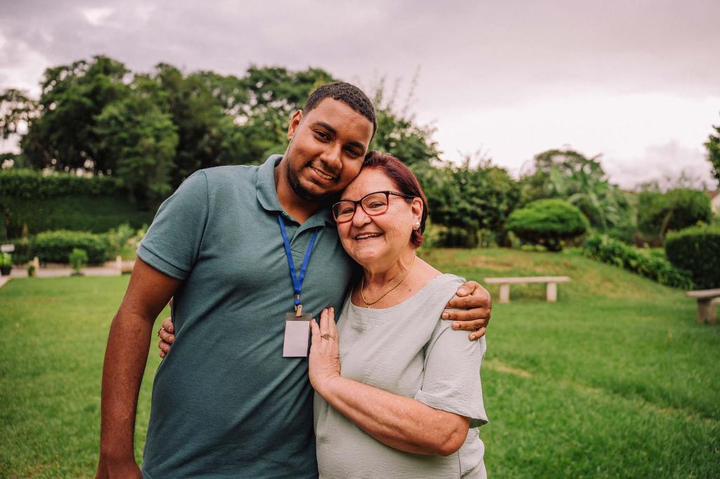 Young man and older woman standing outside posing for a photo while smiling and hugging.